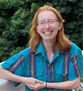 Photo of a red haired woman smiling wearing glasses and a striped turquoise shirt. 
