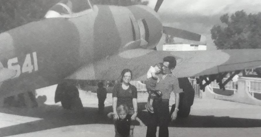 a woman and a man holding a baby, standing in front of a plane