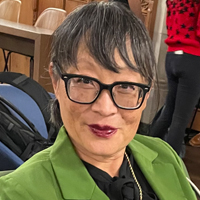 Catherine Liu smiles at the camera while wearing a green suit jacket and glasses. 
