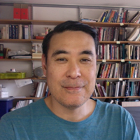 Glen Mimura smiling in front of a full bookshelf. 