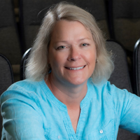 Vicky Johnson sitting in a theater, smiling and wearing a blue blouse. 