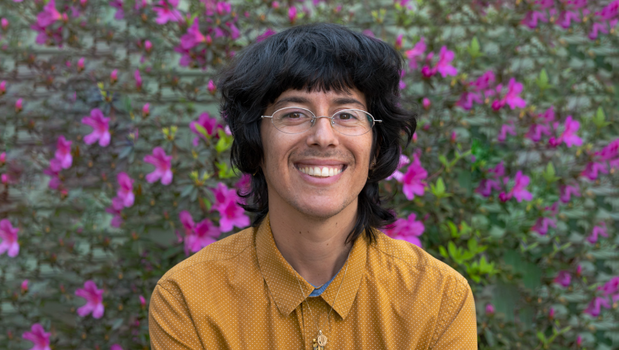 A headshot of Dan Bustillo against a background of magenta flowers and greenery