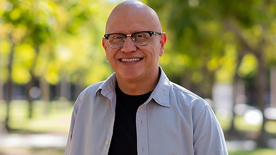 Alex Espinoza smiles; blurred trees fill his background