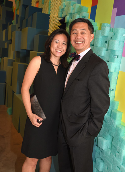 Eileen Chun-Fruto and Richard Fruto pose in elegant attire in front of a colorful wall