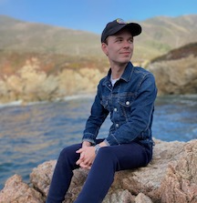 a young person sits on a rock in front of a river and hills