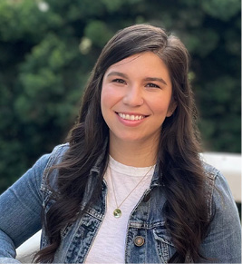 A brunette women in a denim jacket smiling.