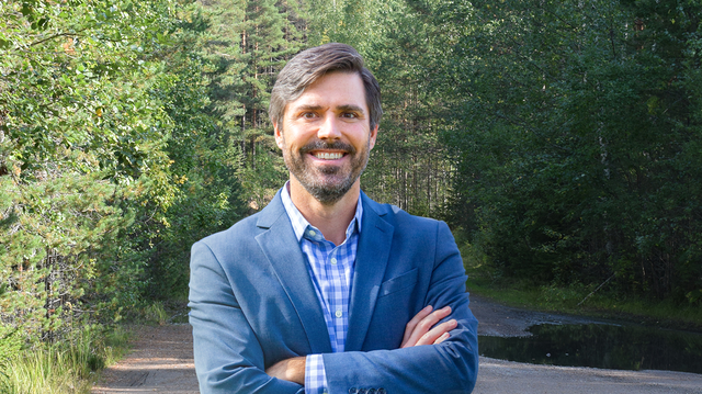 James Nisbet stands before a forest background with his arms crossed; he's smiling