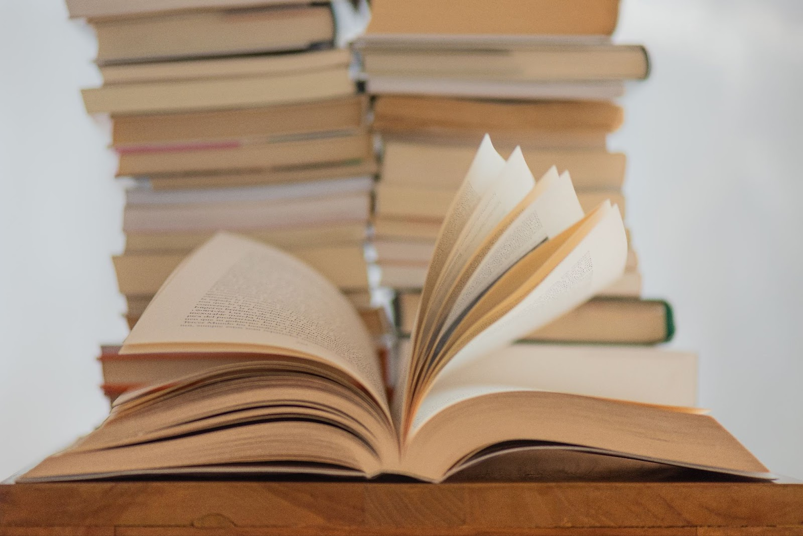 A 2 piles of books in the background with a book in the front, open with pages fluttering