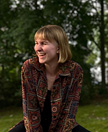 Photo of Jamie Rawn smiling and looking away from the camera in front of green vegetation.