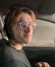 Photo of Joseph Sweetnam wearing glasses and a gray shirt, while sitting in a car
