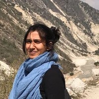 Photo of a smiling woman standing in front of a hill wearing a blue scarf.