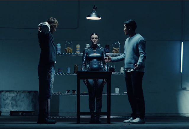 Two men and a robot standing in a dark warehouse