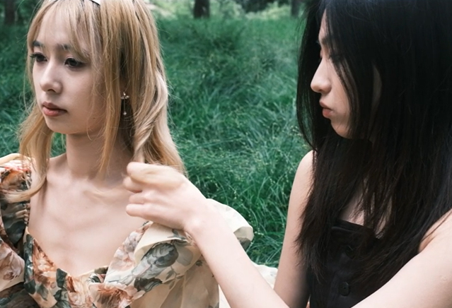 Two woman sit in tall grass. 