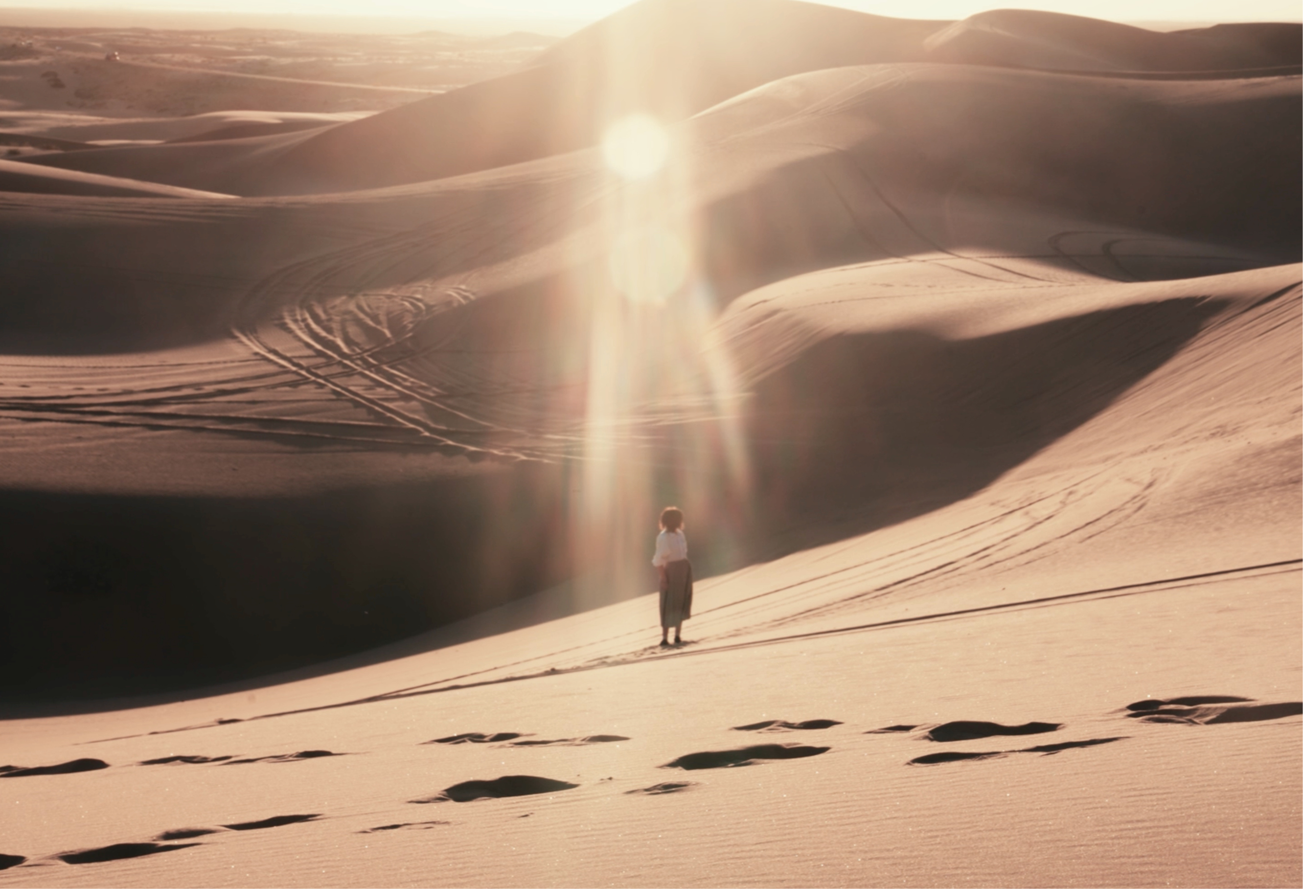 A still from the film Mirage: a figure stands in the middle of endless sand dunes