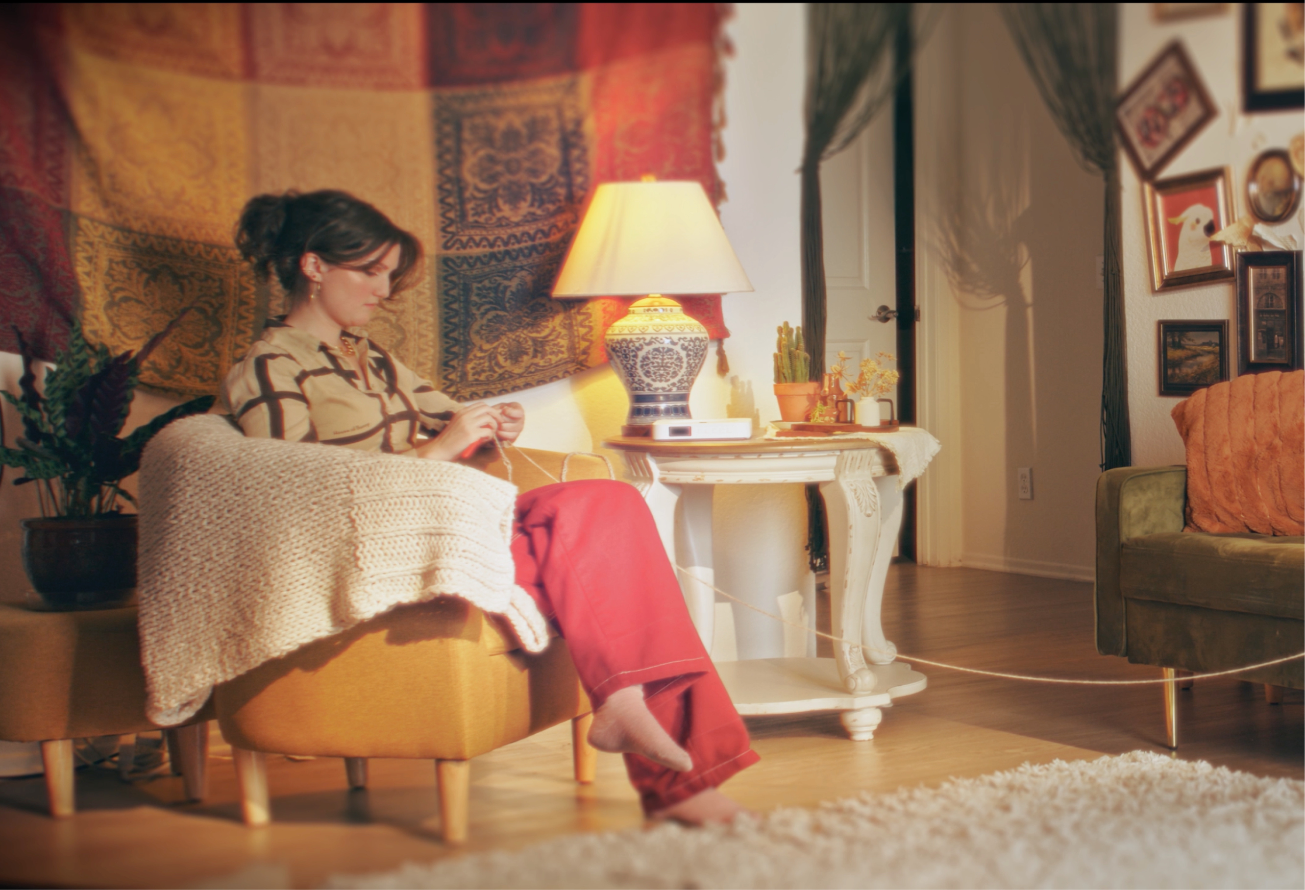 A frame from the film Call Me When You Can't: A woman sits in a decorated living room, knitting. 