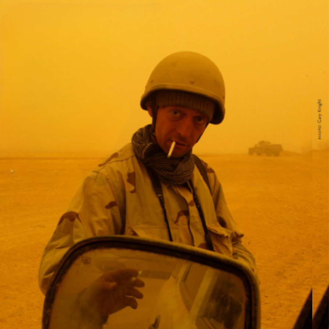 Decorative image of  soldier standing in the middle of a desert in front of a  vehicle 
