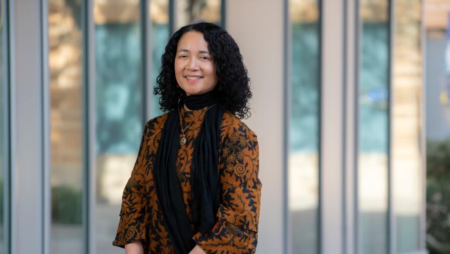 Fatimah Tobing Rony wears a black and orange patterned top and black scarf. She is front of Humanities Gateway at UCI