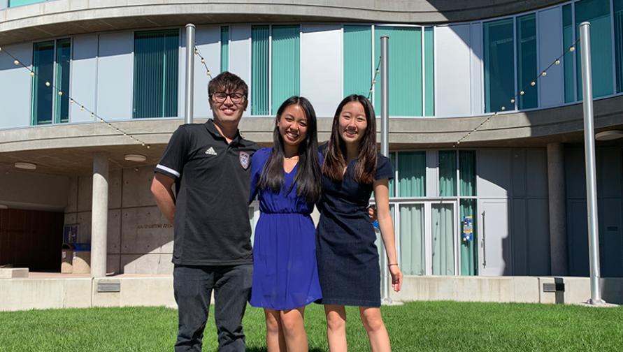 Three literary journalism students pose for a photo in front of Humanities Gateway