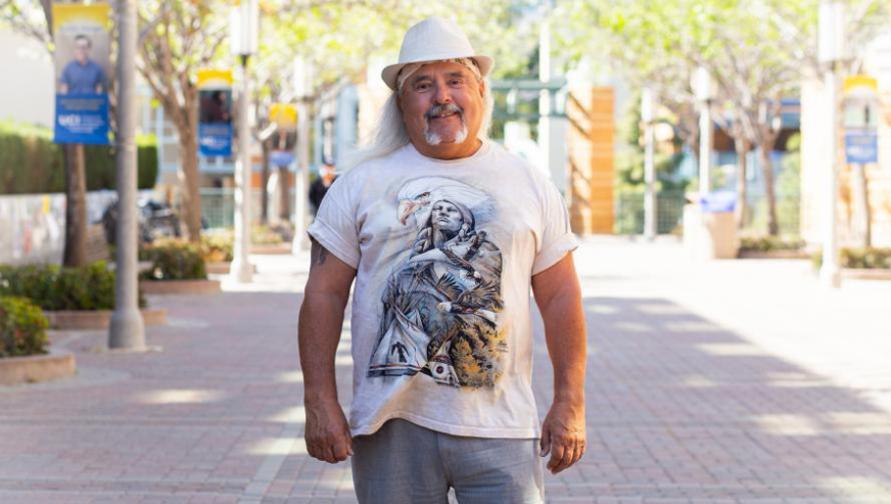 Al Encinias wears a white graphic T-shirt and a white fredora