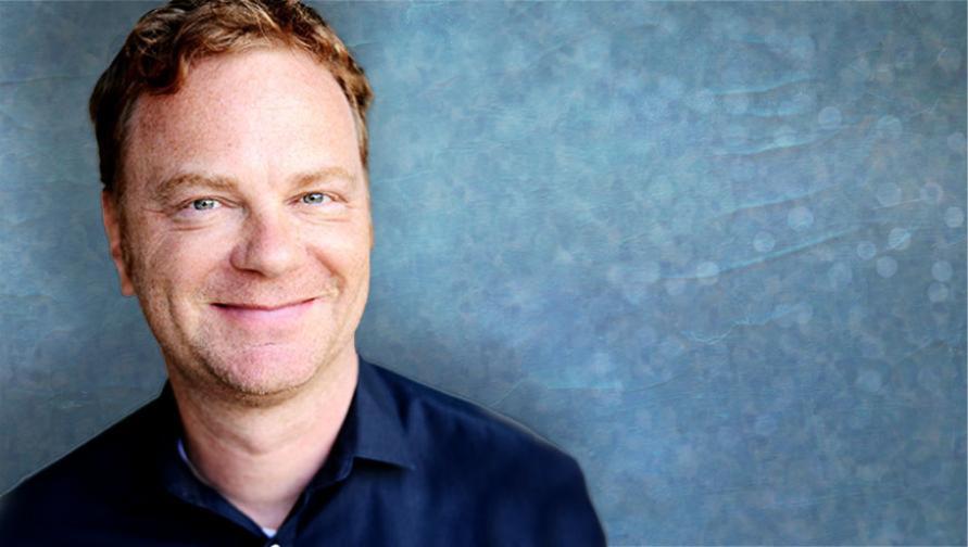 A headshot of Peter Krapp against a bluish gray background