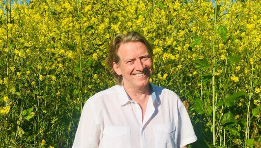 A portrait of Joseph McKenna in front of a tall field of yellow flowers