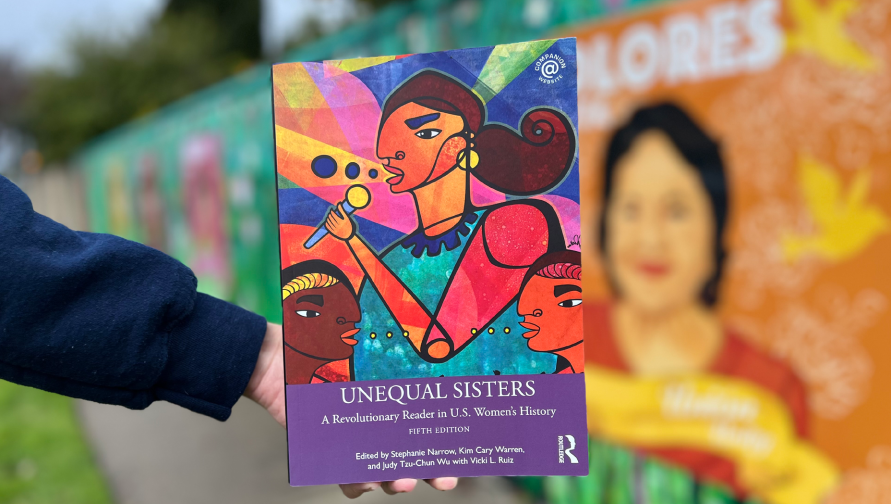 The book Unequal Sisters is held in front of a mural background