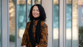 Fatimah Tobing Rony wears a black and orange patterned top and black scarf. She is front of Humanities Gateway at UCI