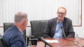 Tyrus Miller sits at a table set up with microphones alongside Mark Lazenby