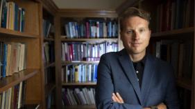 Duncan Pritchard poses with his arms crossed inside a library