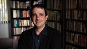 A portrait of Alex Borucki with bookshelves in the background.