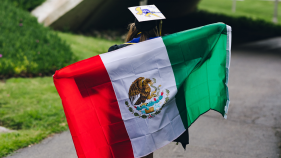 Chelsea Salinas holding a Mexican flag across her back as she walks away from the camera.