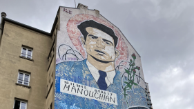 Mural on the side of a building showing a painting of Missak Manouchian wearing a blue suit with a red halo around his head.