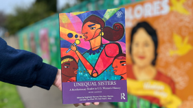 The book Unequal Sisters is held in front of a mural background