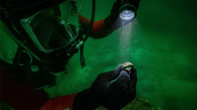 Scuba diver holding up a shining object and looking at it with a flash light.