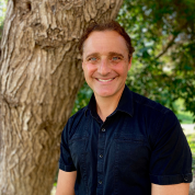 John Gamber smiling next to a tree trunk