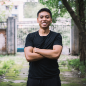 Sheldon Chau standing in front of a gate with trees on the side with his arms crossed