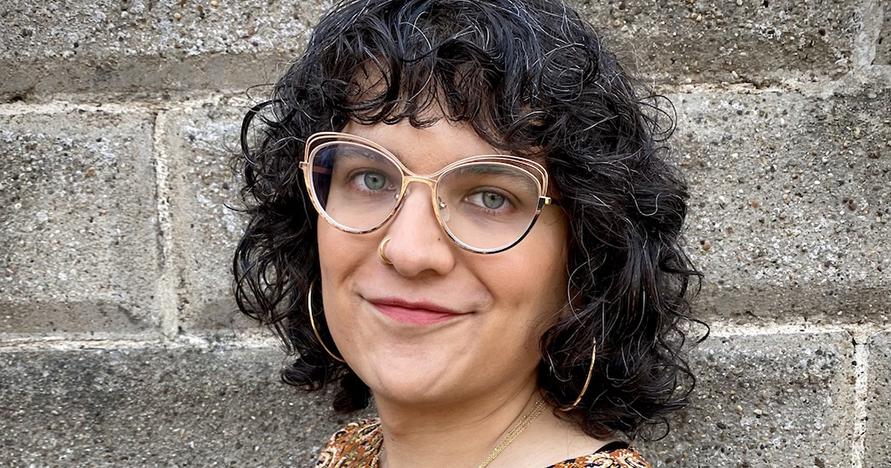 Face of smiling person with dark curly hair and glasses