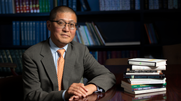 Jim Lee sits at his desk, with a stack of books placed next to him