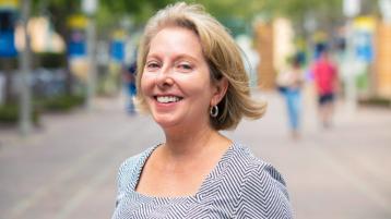 Head and shoulders of smiling woman outside on campus walkway