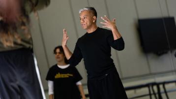 male dancer in black shirt and black pants with hands lifted to shoulders