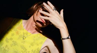 woman against black background with hand covering her face