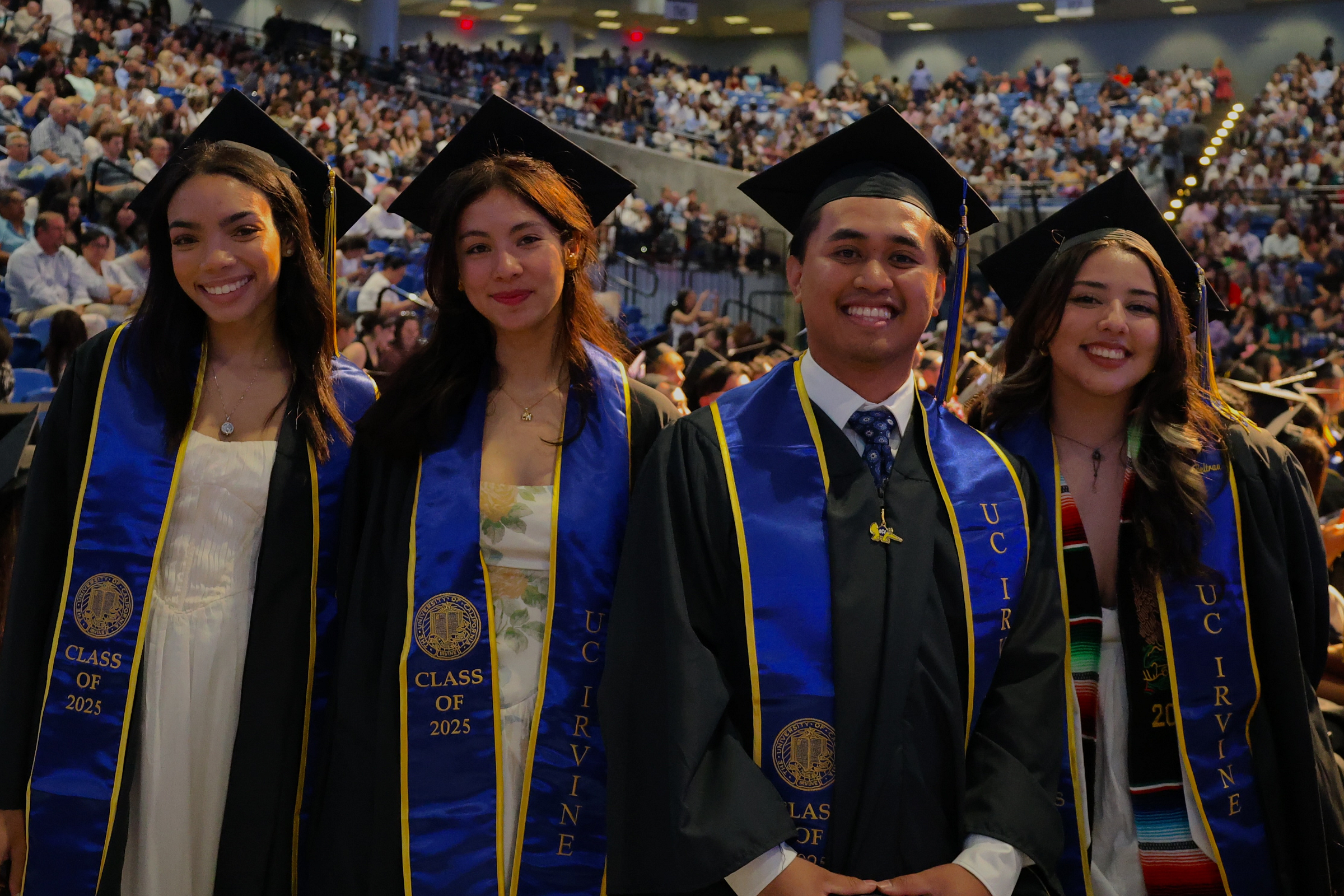 Four students, wearing graduation caps and gowns smile for the camera