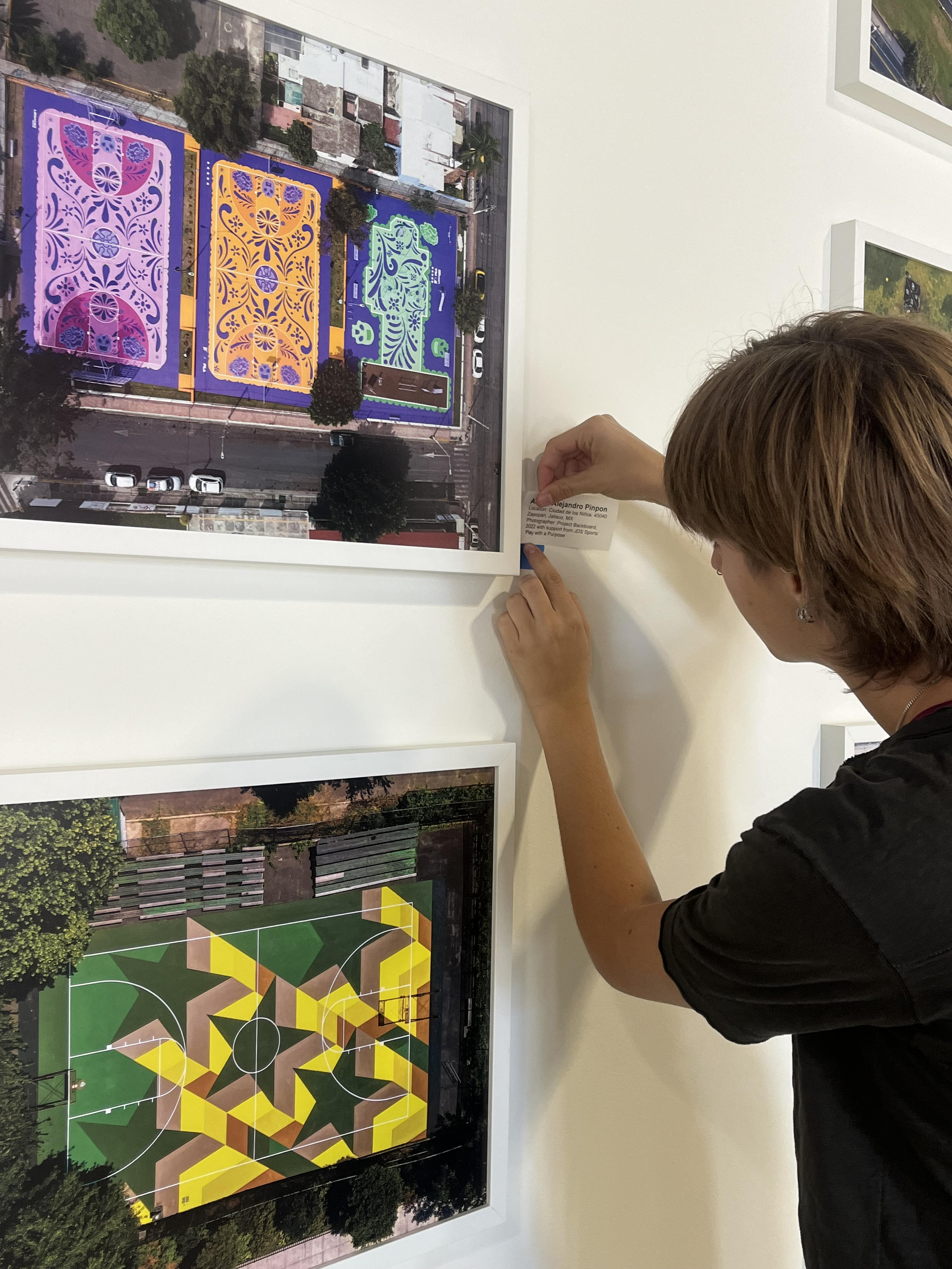 Alessandra is pinning up a description paper for a piece of artwork on a wall.