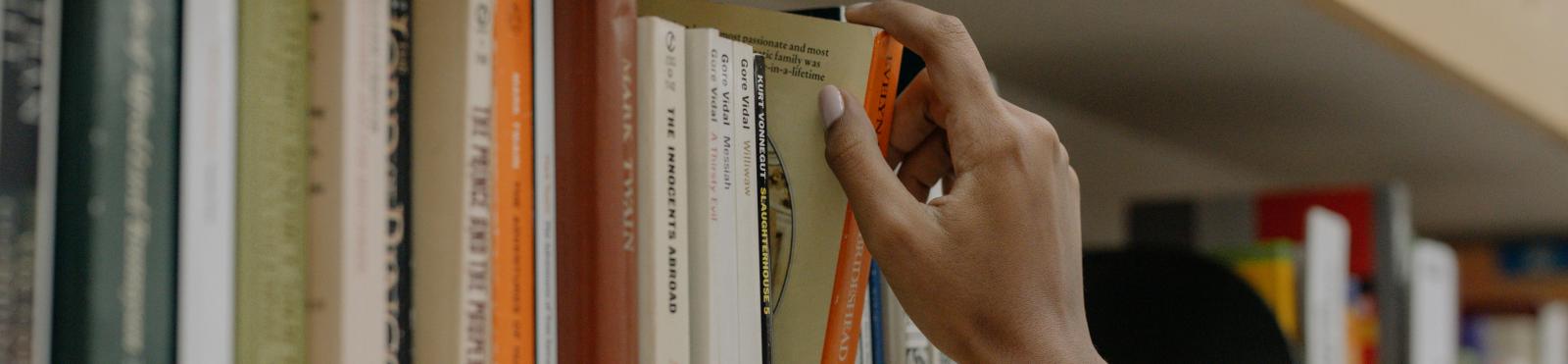 A person reaching for a book on a shelf
