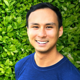 Andrew Almendras smiling in front of a hedge