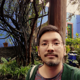 Keiji Kunigami with trees and bushes with a building in the back