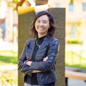 Woman with black hair wearing black leather jacket, standing with arms folded