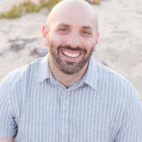 Smiling man with beard and striped shirt sitting on sand dune