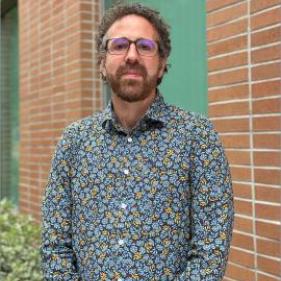 Man with brown curly hair wearing glasses and print collared shirt