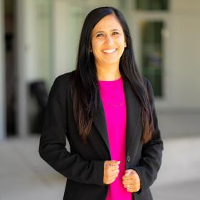 Shabnam Malek-Cazares smiling, wearing a black blazer and pink top.
